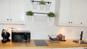 A kitchen with white cabinets, a black microwave, a coffee maker, a sink, and potted plants on the wall. - Rosablanche D12 by Interhome (Siviez-Nendaz)