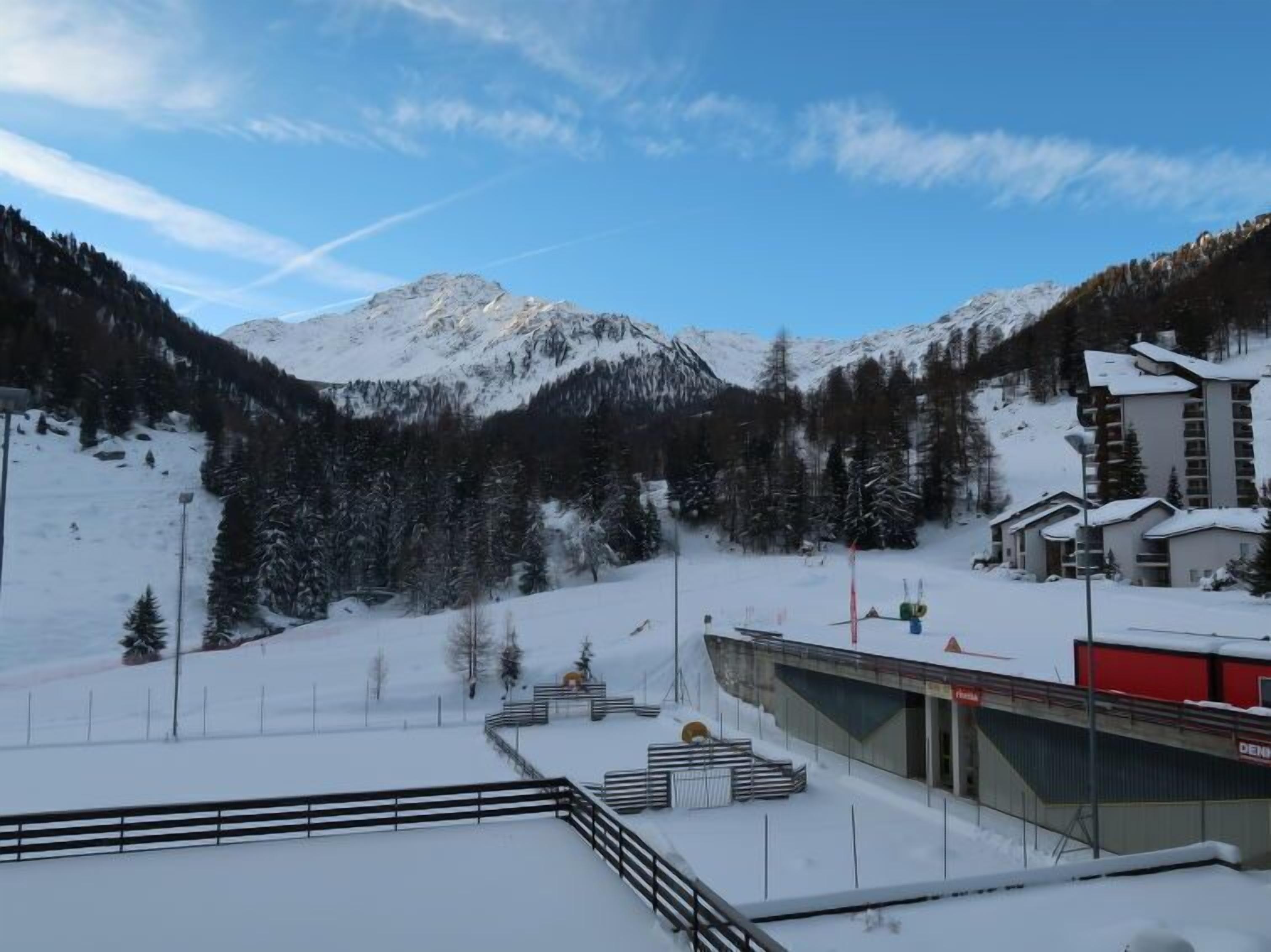 A snow-covered mountain landscape with a ski resort building featuring a red and white facade, a ski lift, and a mountain view.