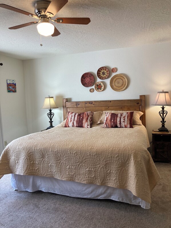 Un dormitorio con cabecera de madera, una cama grande con ropa de cama estampada, dos lámparas de noche y decoración en la pared que incluye platos tejidos.