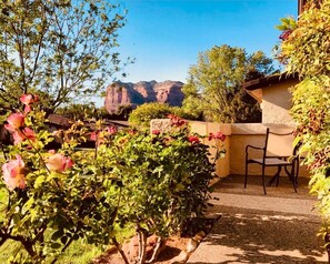 Un patio con una silla, rodeado de plantas en flor y vistas a formaciones rocosas rojas.