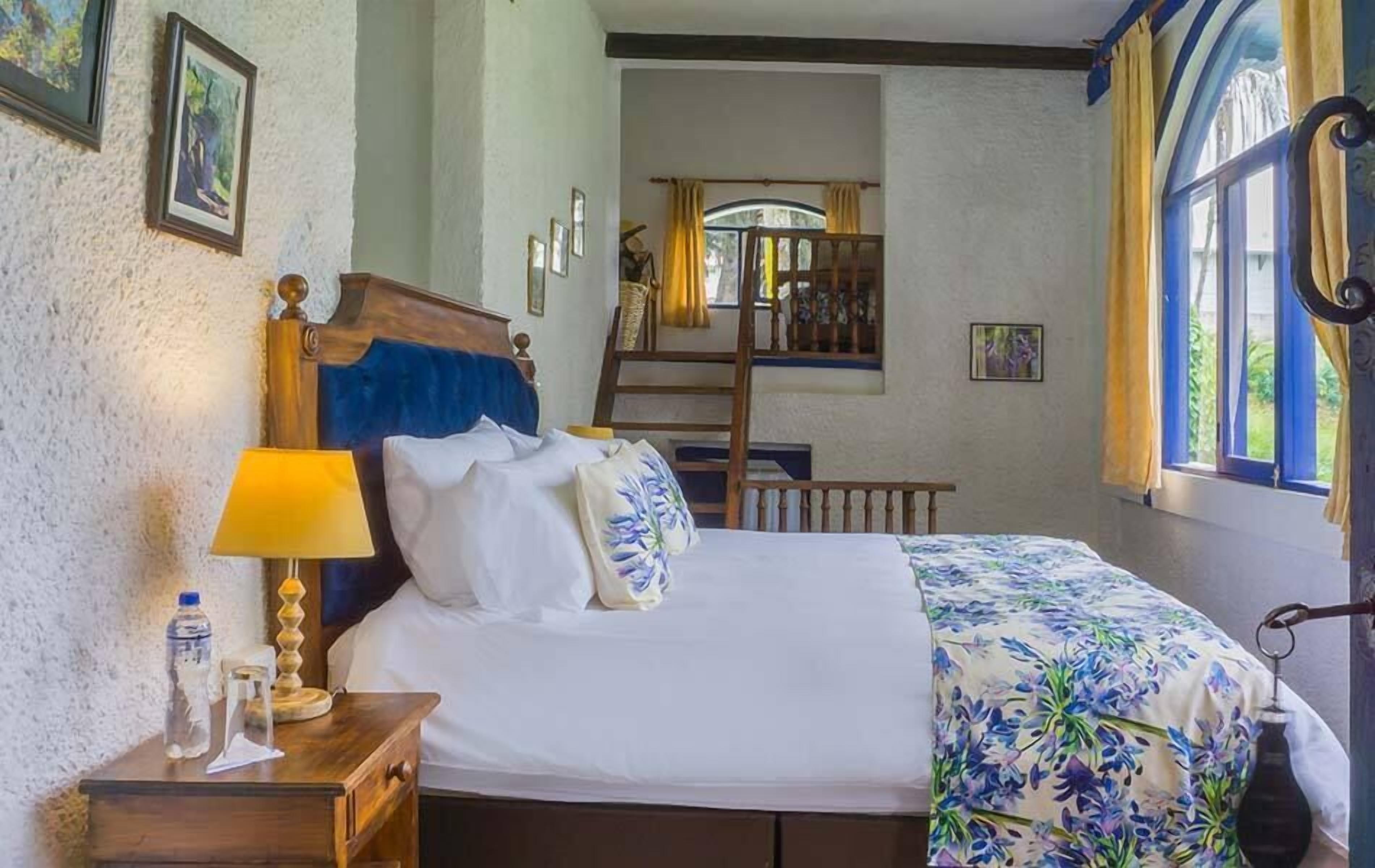 A bedroom with a wooden bed, a nightstand with a lamp, and a window with curtains.