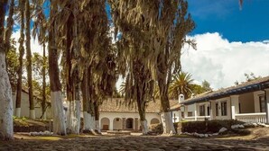 A courtyard with stone paving, white-painted trees, and a building with a tiled roof. - Hosteria Hacienda Pinsaqui (San Juan de Ilumán)