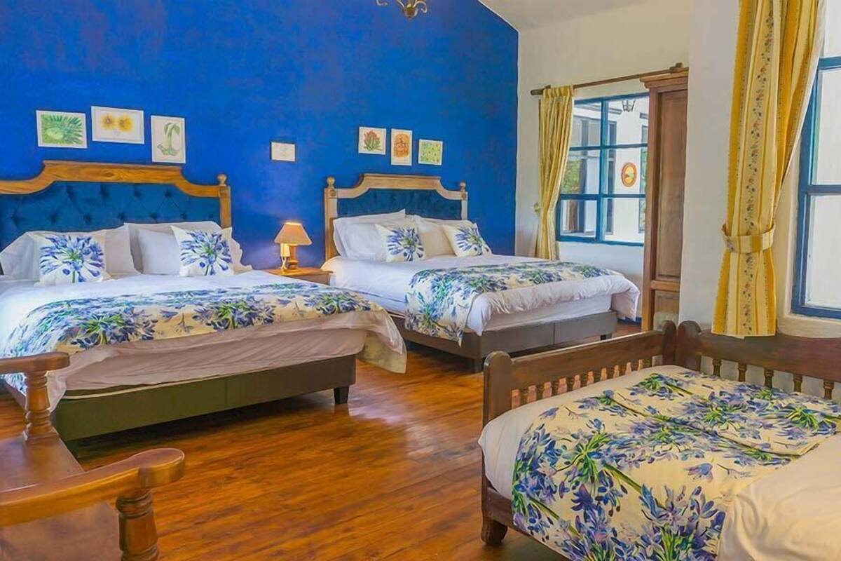 Une chambre d’hôtel avec deux lits, des têtes de lit en bois, des couvre-lits à motifs floraux et un plancher en bois.