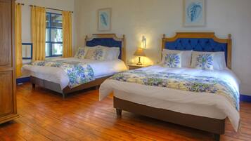 Two double beds with floral bedding, wooden headboards, and a wooden floor.