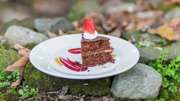 A slice of chocolate cake with a strawberry on a white plate, placed on a moss-covered rock.