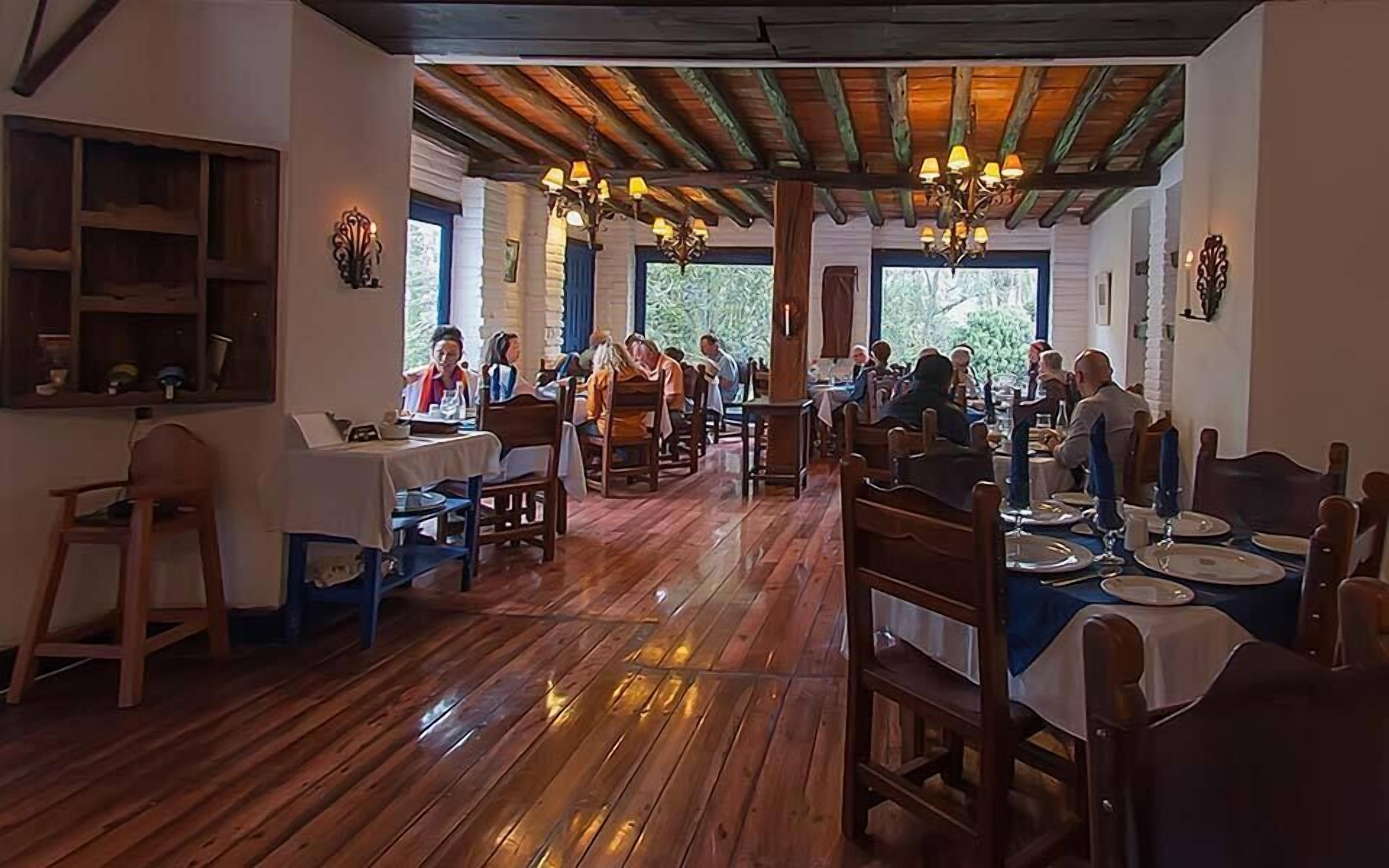 Un restaurante con suelos y mesas de madera, ventanas amplias y candelabros.