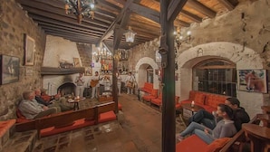 A rustic interior with stone walls, wooden beams, a fireplace, and a seating area with red cushions. - Hosteria Hacienda Pinsaqui (San Juan de Ilumán)