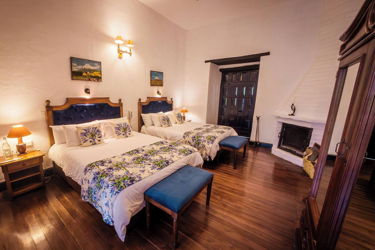 Une chambre d’hôtel avec deux lits, un plancher en bois, une cheminée et des œuvres d’art accrochées aux murs.