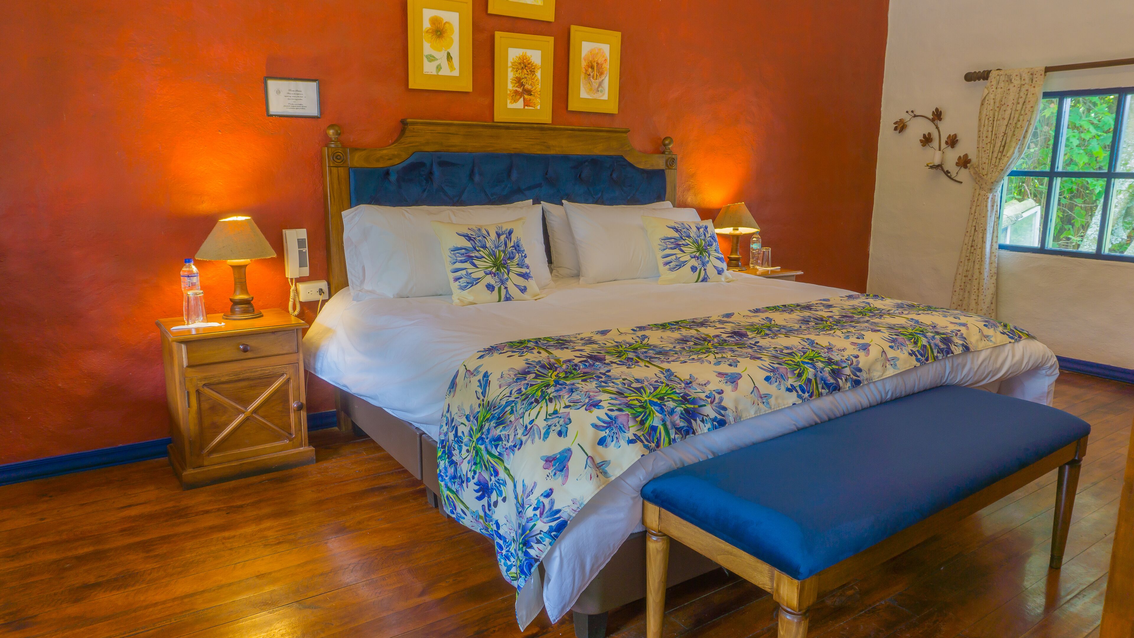 A neatly made bed with floral bedding, a bedside table with a lamp, and a bench.