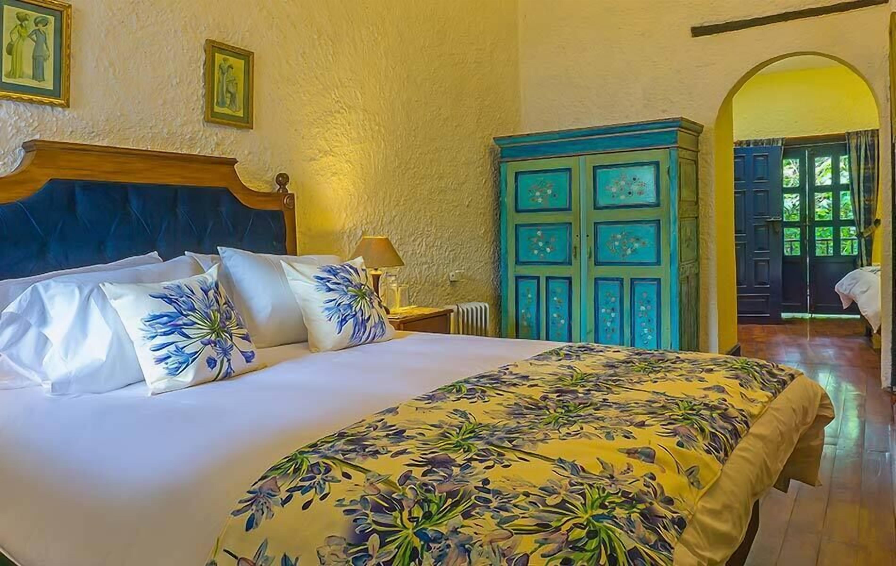 Un dormitorio con una cama grande, cabecera de madera, colcha estampada y un aparador azul.
