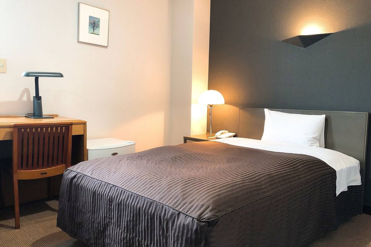 A hotel room with a bed, bedside table, lamp, and a framed picture on the wall.