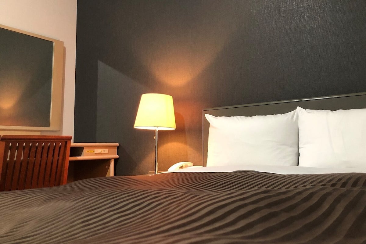 A hotel room with a bed, a nightstand, a lamp, and a wall-mounted TV.