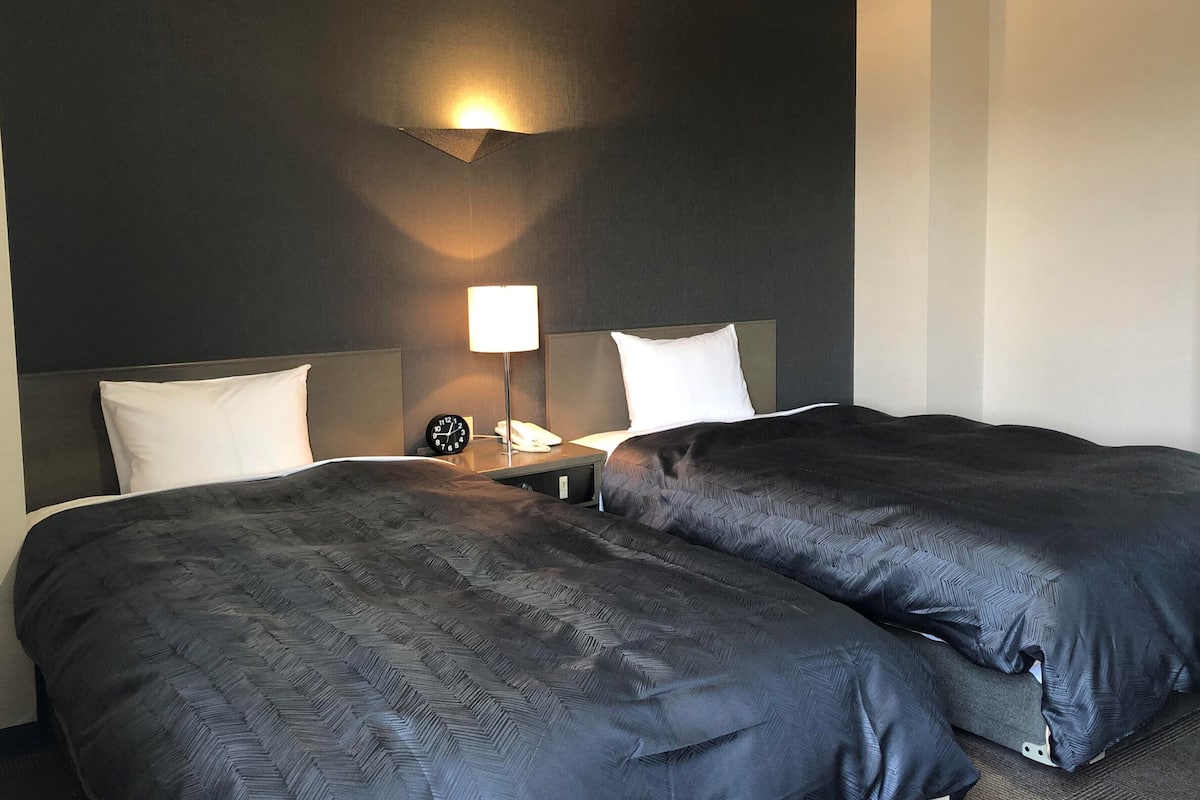A hotel room with two beds, a nightstand, a lamp, and a clock.