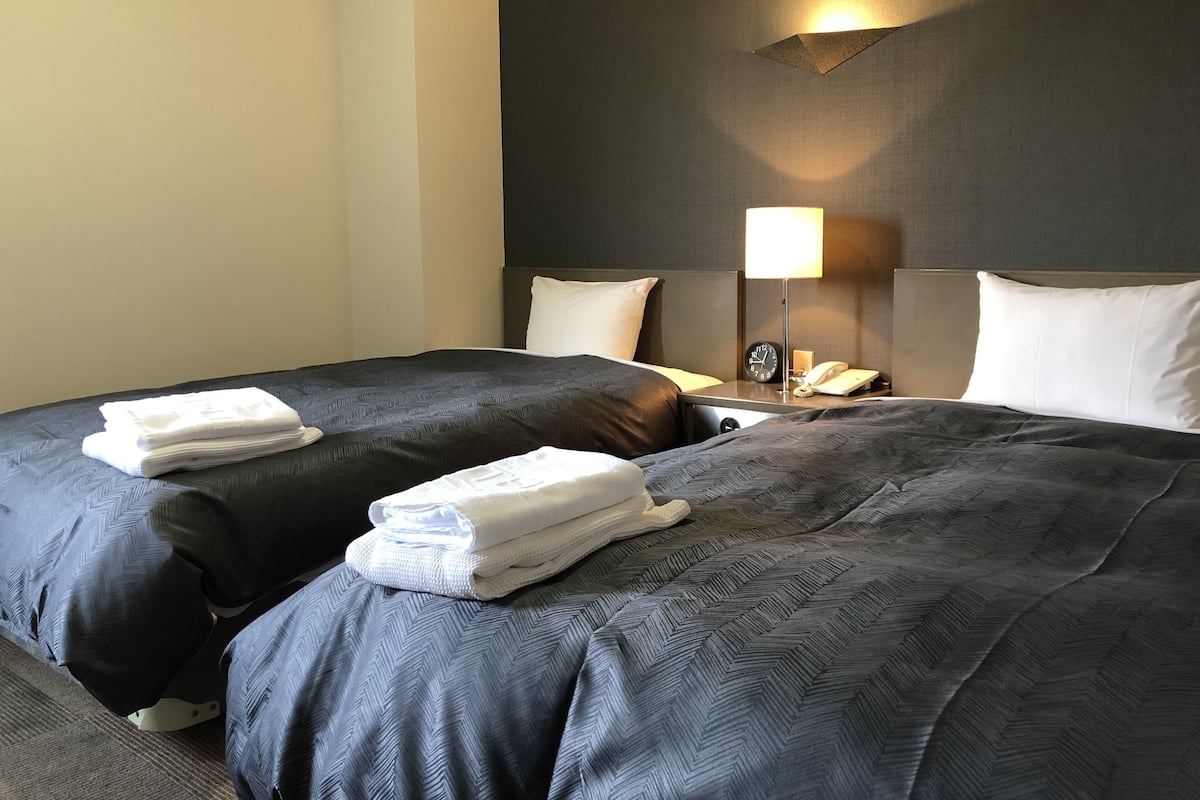 A hotel room with two beds, a nightstand with a lamp, and a telephone.