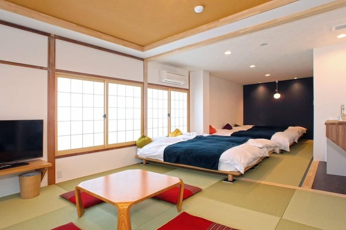 Una habitación tradicional japonesa con suelo de tatami, televisor, cama con muchas almohadas y una mesita.