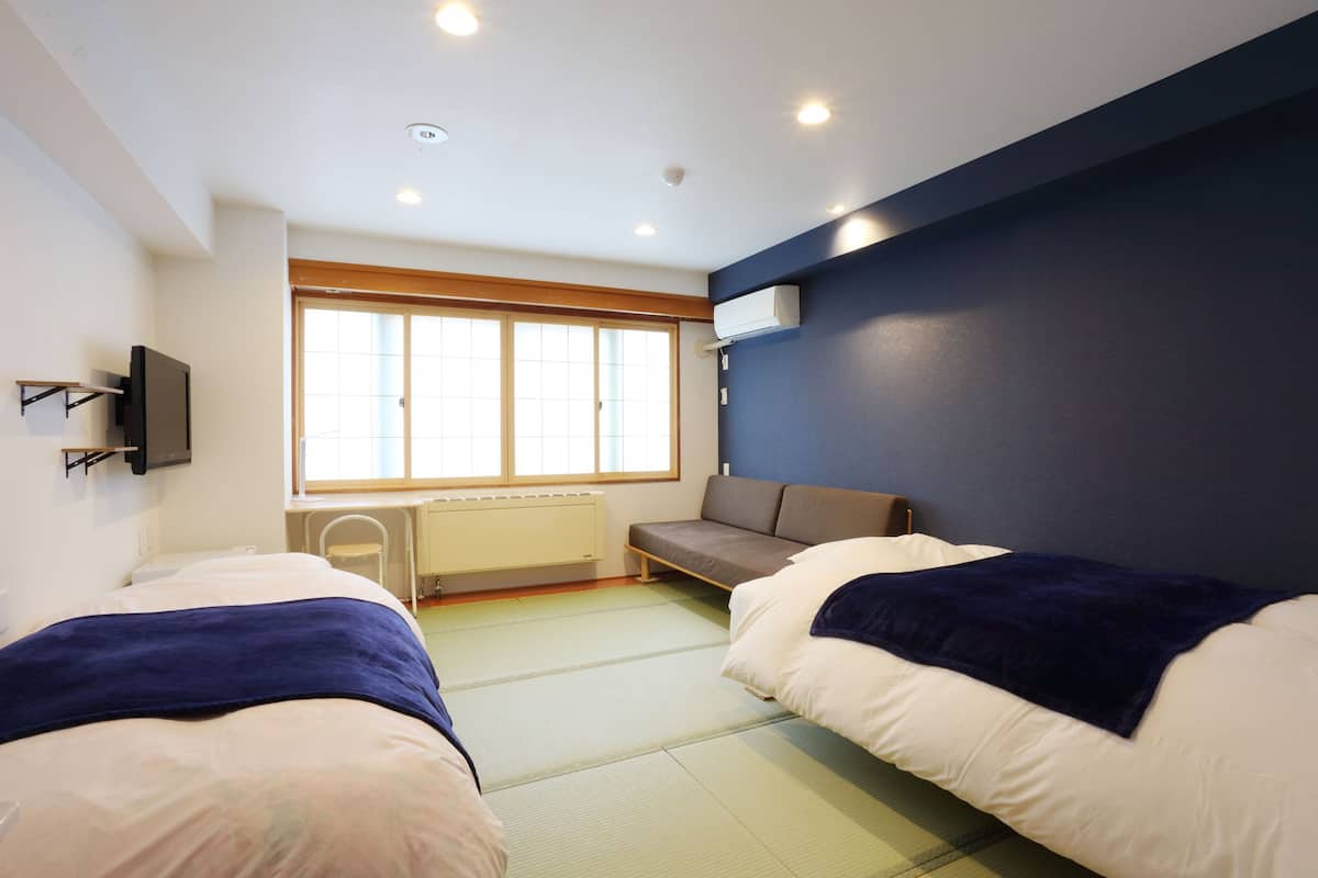 Una habitación con dos camas, una ventana, un radiador y un televisor instalado en la pared.