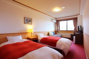 A hotel room with two beds, a bedside lamp, a television, and a window with curtains.