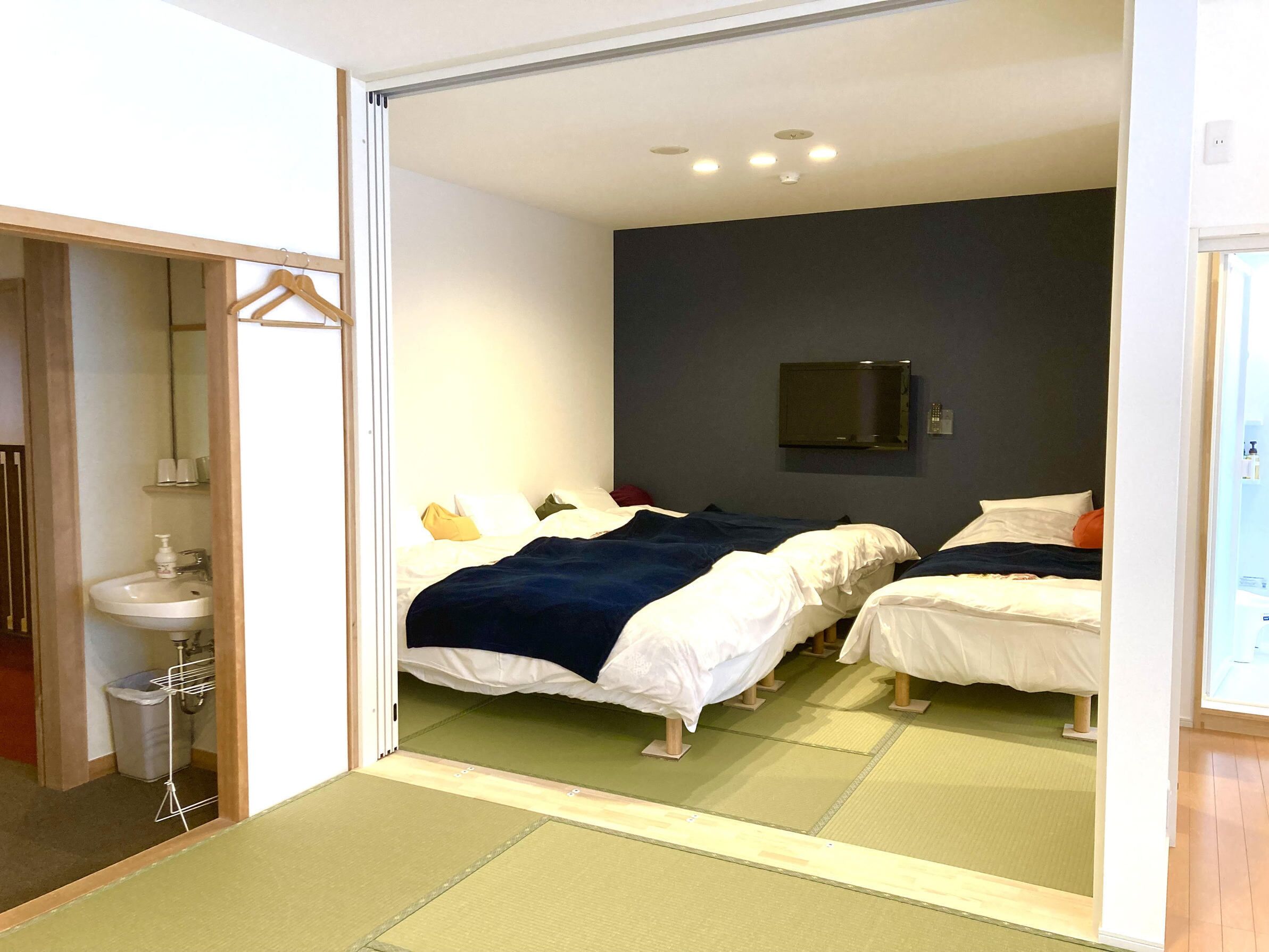 Hotellihuone, jossa on kaksi sänkyä, pesuallas, peili ja televisio.