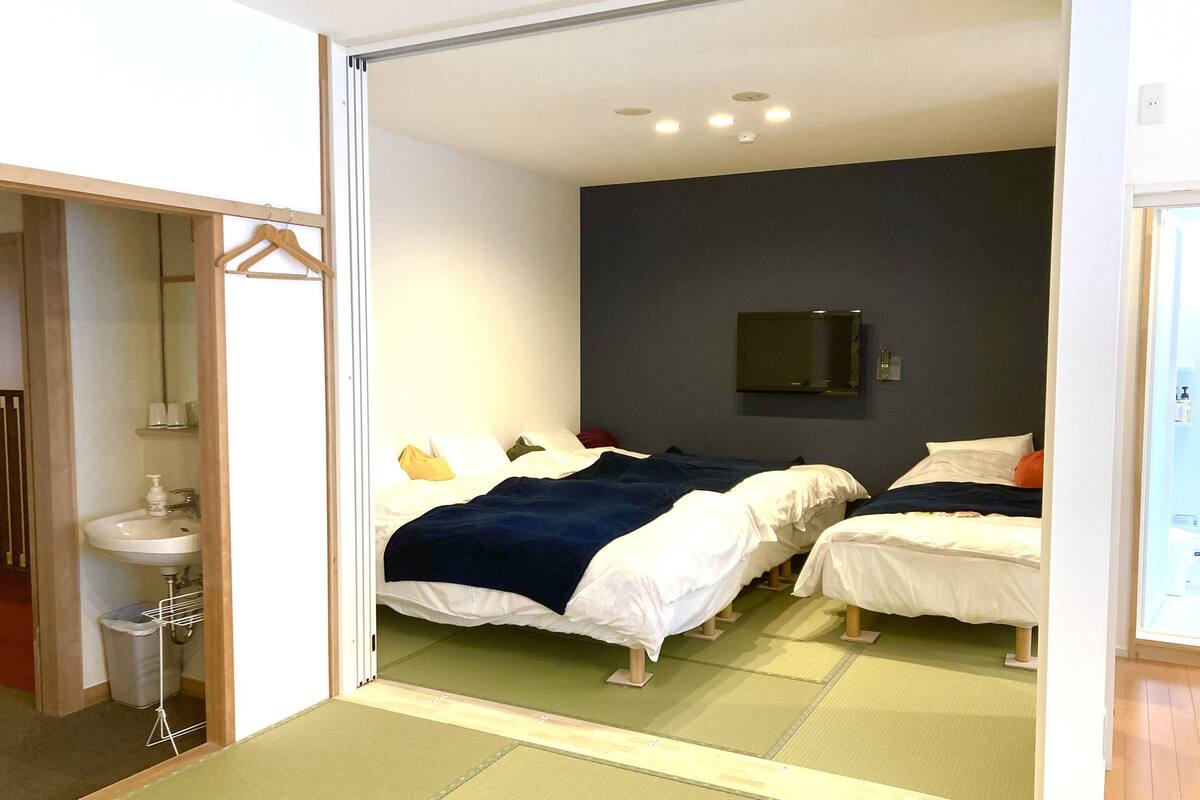 Habitación de hotel con dos camas, un lavamanos, un espejo y una televisión.