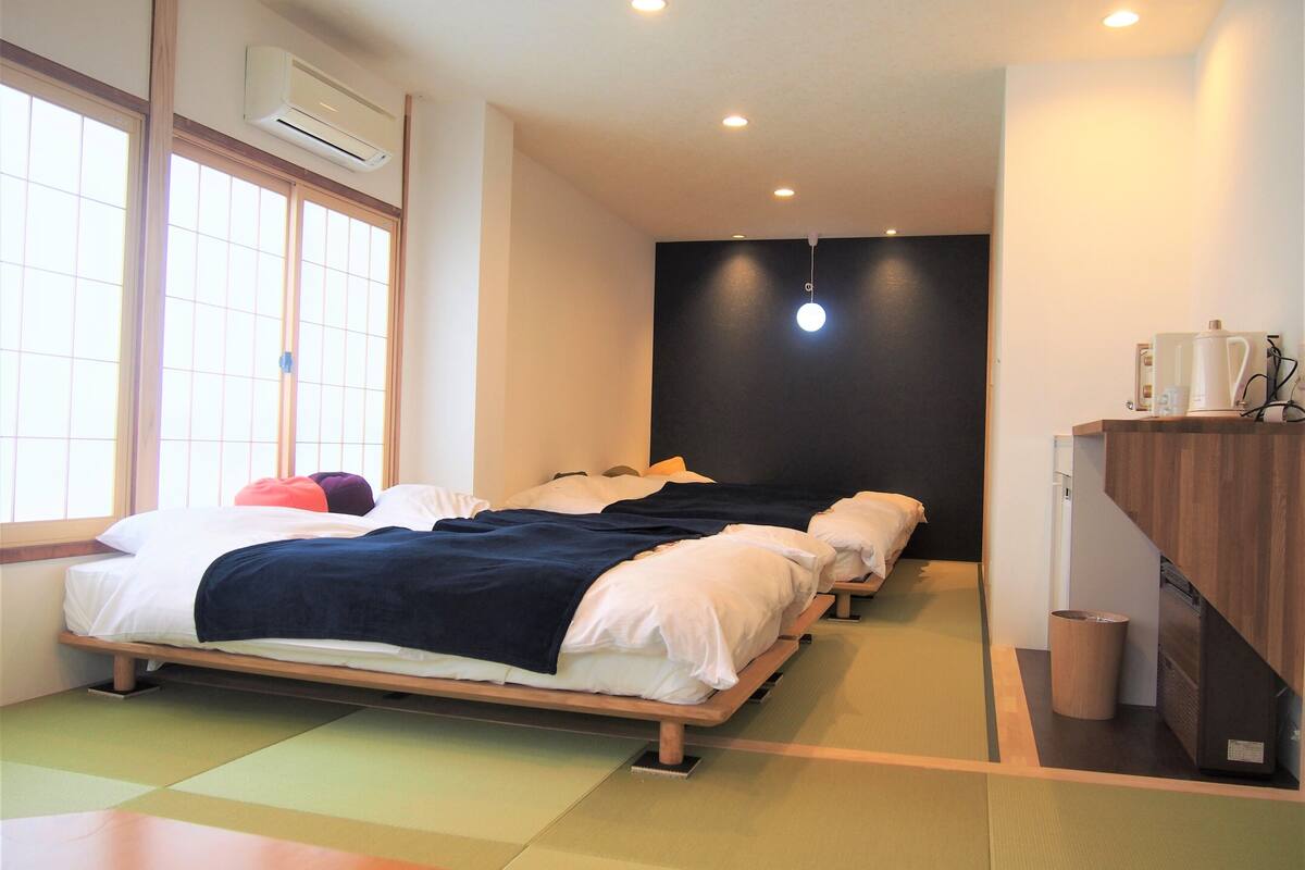 Una habitación de hotel con cama, una mesita, un cubo de basura y una zona de kitchenette.