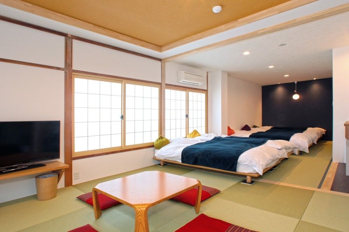 Une pièce de style japonais traditionnel, avec un sol recouvert de tatamis, une télévision, un lit avec plusieurs oreillers et une petite table.