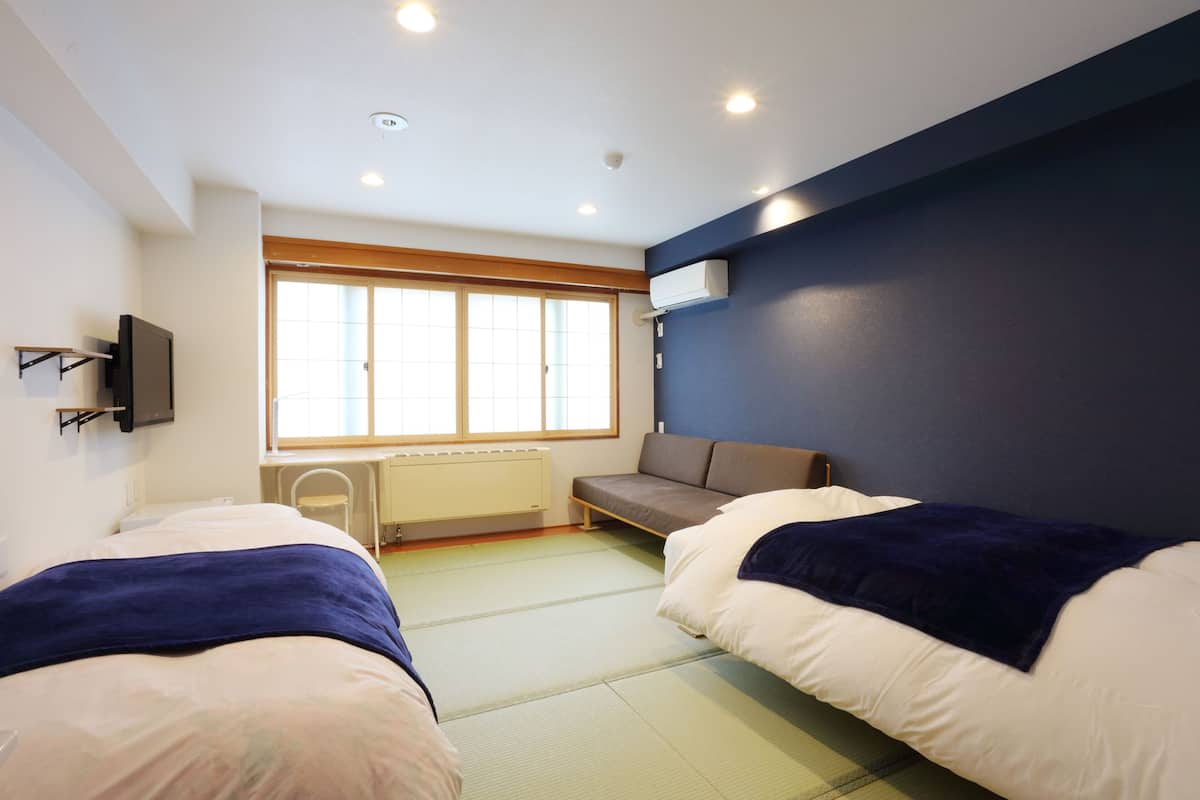 Una habitación con dos camas, una ventana, un radiador y un televisor de pared.