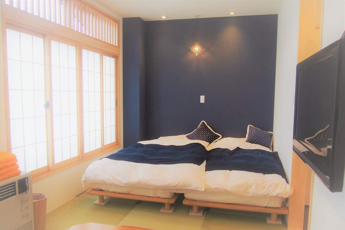 Una habitación con dos camas, una ventana con persianas, una lámpara colgante y una pequeña mesa.