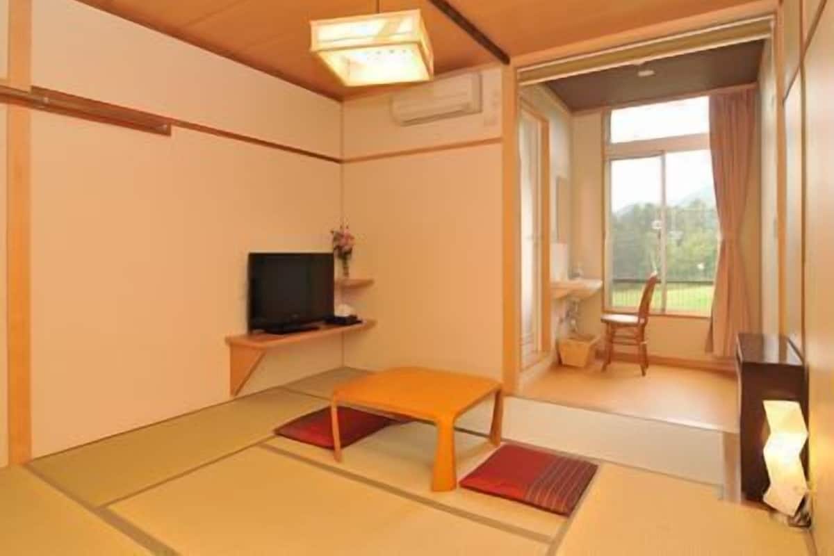 Una habitación con suelo de tatami, televisión, una mesita y una ventana con cortinas.
