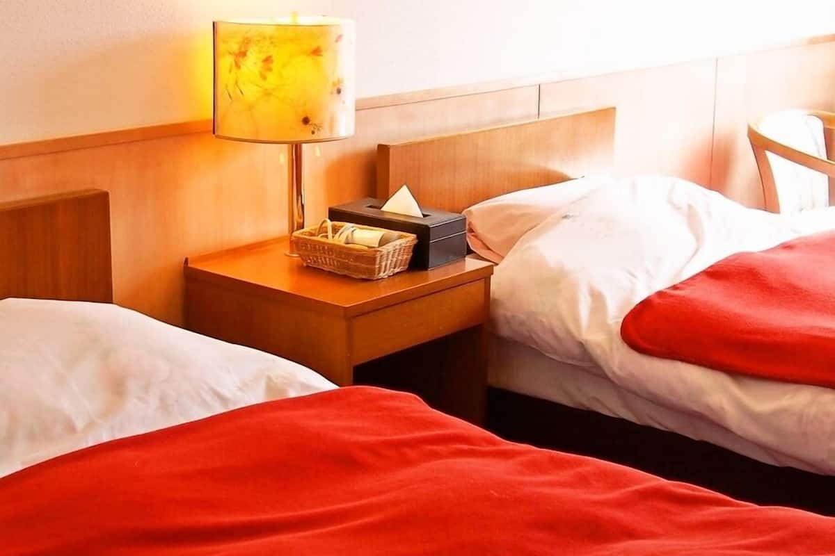 Una habitación de hotel con dos camas, una mesita de noche con lámpara y una cesta.
