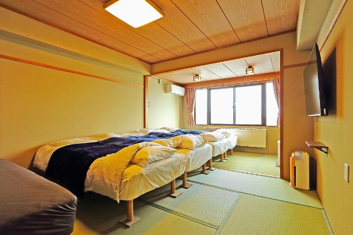 Una habitación con una cama grande, un ventanal, un televisor montado en la pared y un radiador.