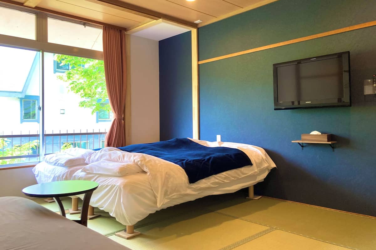 Habitación de hotel con cama, una mesita, televisor montado en la pared y ventana con cortinas.