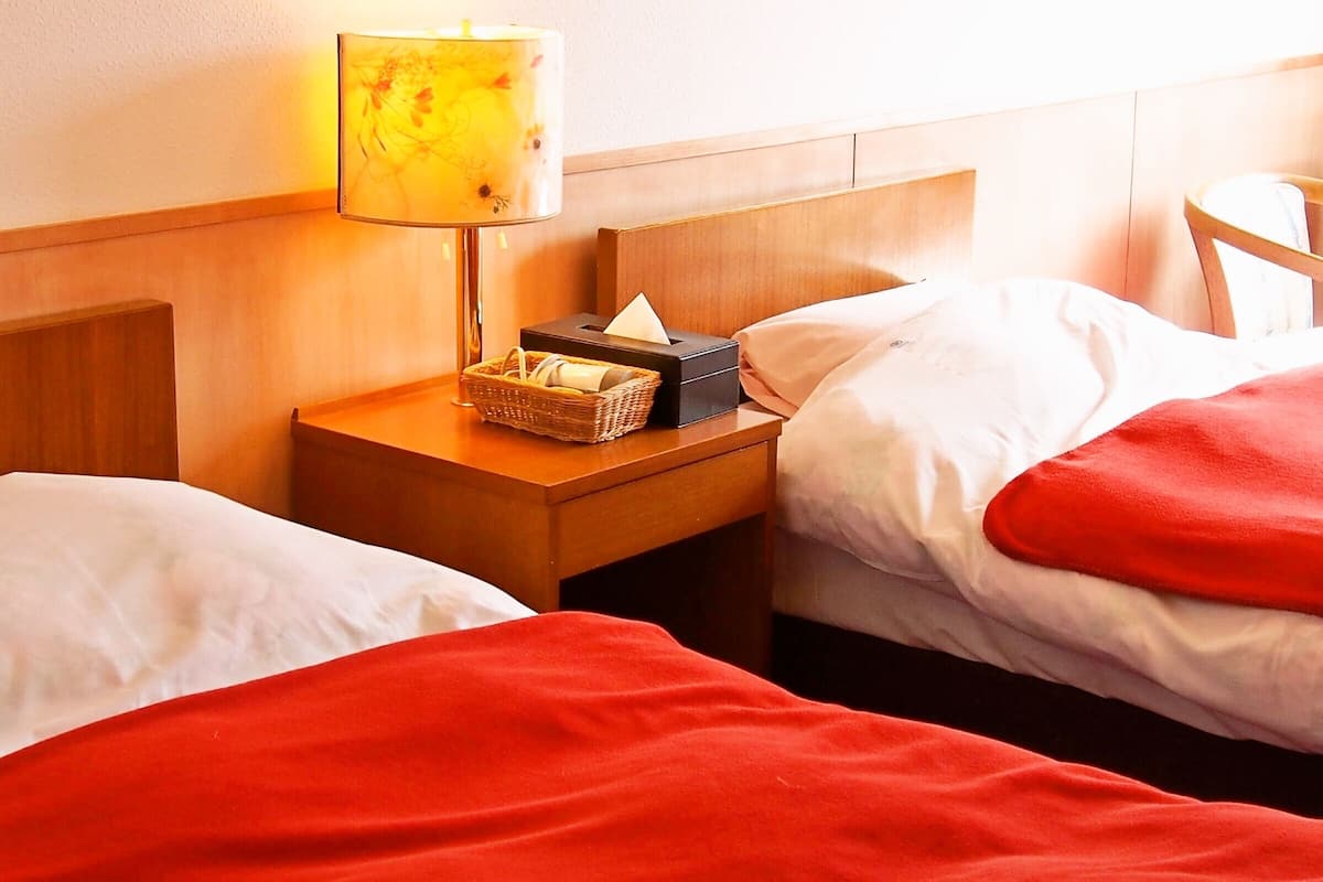 Una habitación de hotel con dos camas, una mesita de noche con lámpara y un cabecero de madera.