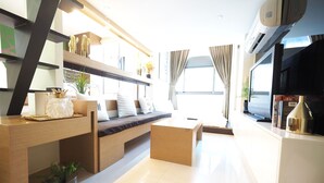 A modern living room with a sofa, coffee table, and a TV. There is a bookshelf with decorative items and a window with curtains. - 5MIN to ATT 4 FUN (Taipei)