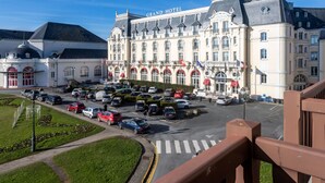 Un grande hotel con una facciata imponente, diverse bandiere e un parcheggio con varie automobili.