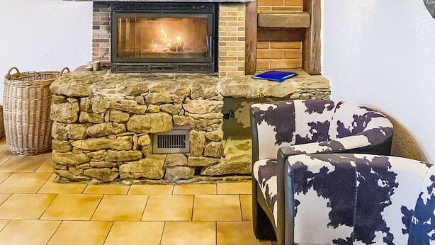 A stone fireplace with a fire, a blue book on the mantel, and a patterned armchair.