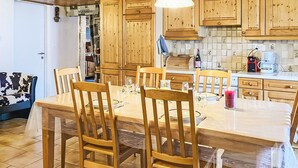 A wooden dining table with chairs, a kitchen area with wooden cabinets, a refrigerator, and a coffee maker.