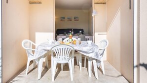 Un comedor con una mesa dispuesta para cuatro personas, rodeada de sillas blancas, y vistas a una cocina al fondo.