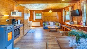 A cozy cabin interior with wooden walls and ceiling, a kitchenette, a sofa, a dining table, and a TV.