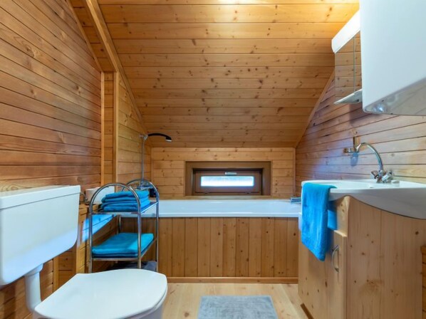 A compact wooden cabin bathroom with a sink, toilet, and a window above the sink.