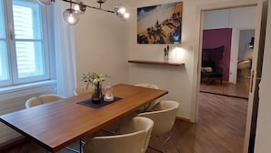 Un coin repas avec une table en bois, des chaises blanches, un vase rempli de fleurs et un tableau accroché au mur.
