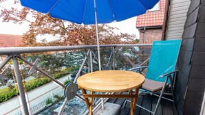 Un balcon avec une table et des chaises en bois, un parasol bleu et une vue sur une rivière et des bâtiments.