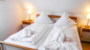 Un lit double avec du linge de lit blanc, deux oreillers et deux serviettes enroulées. Il y a deux tables de chevet avec des lampes.