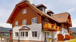 A large, two-story wooden house with a balcony, a chimney, and a well-maintained lawn.