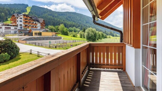 A wooden balcony with a view of a mountain landscape and a building with multiple floors.