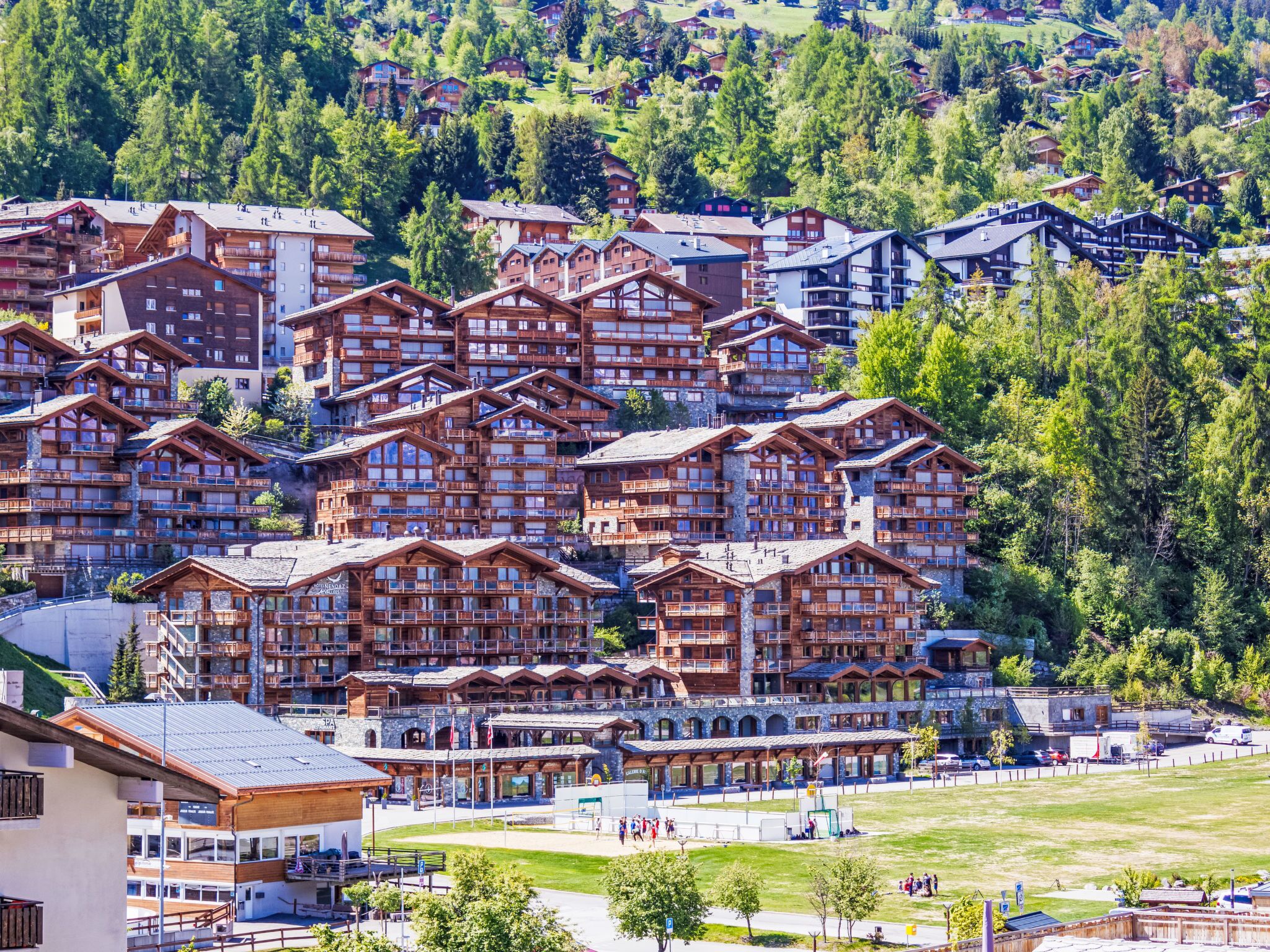 A cluster of wooden chalet-style buildings with balconies, set against a backdrop of green hills.