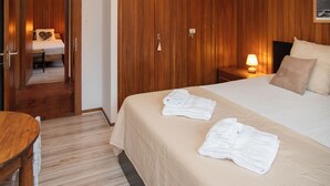 A hotel room with a wooden wardrobe, a bed with a beige bedspread, two bedside tables with lamps, and a wooden desk. - Val Neige 11 by Interhome (Verbier)