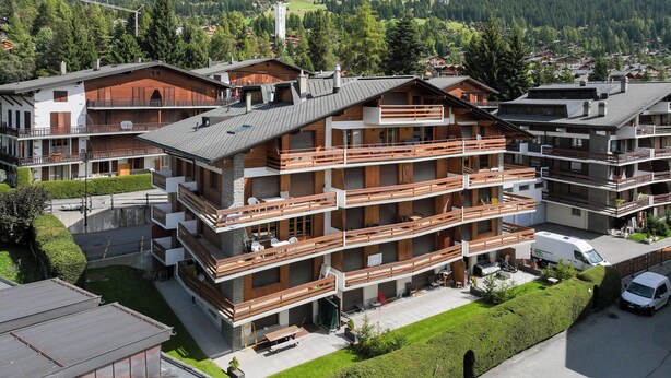 A multi-story hotel with balconies, a parking area, and a mountainous backdrop. - Val Neige 11 by Interhome (Verbier)