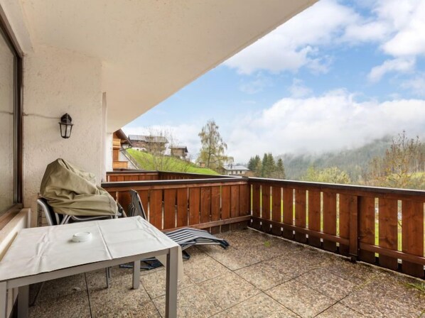 Ein Balkon mit Tisch und Stühlen, einem Hollerleger und Blick auf eine gebirgige Landschaft.