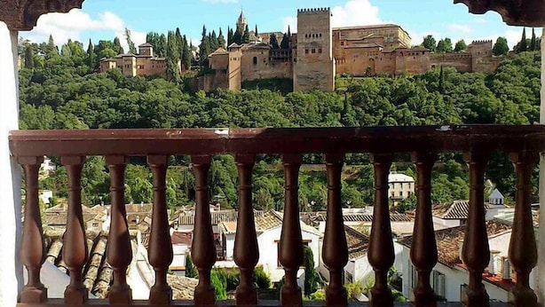Un balcon offrant une vue sur un château historique, entouré de verdure.