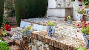 Une cour avec des marches en pierre menant à un bâtiment blanc, entouré de plantes en pot et d’un mur de pierre.